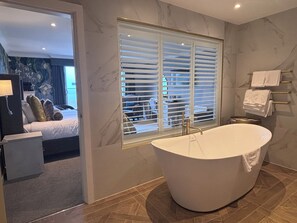 Une salle de bain moderne avec une baignoire sur pieds, une grande fenêtre avec stores et un porte-serviettes.