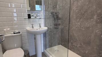 Un bany amb un vàter blanc, un lavabo amb pedestal i una dutxa amb envàs de vidre.