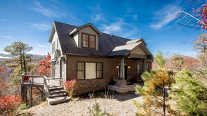 A two-story house with a stone facade, a wrap-around porch, and a small deck. - Burnt Ridge Retreat | Luxury Black Mountain Home w/ Game Room & Mountain Views (Black Mountain)