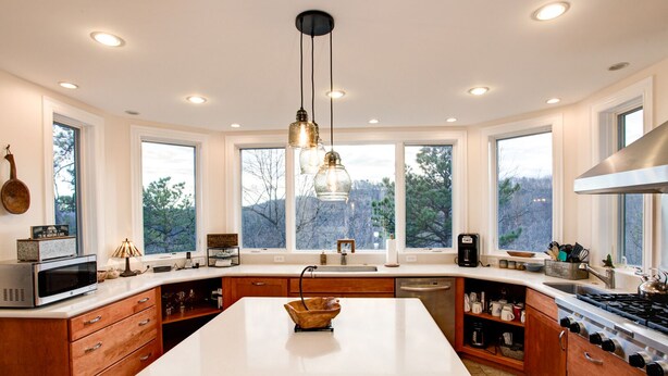 A modern kitchen with a large island, wooden cabinetry, a stainless steel stove, and a view of the outdoors through large windows. - Burnt Ridge Retreat | Luxury Black Mountain Home w/ Game Room & Mountain Views (Black Mountain)