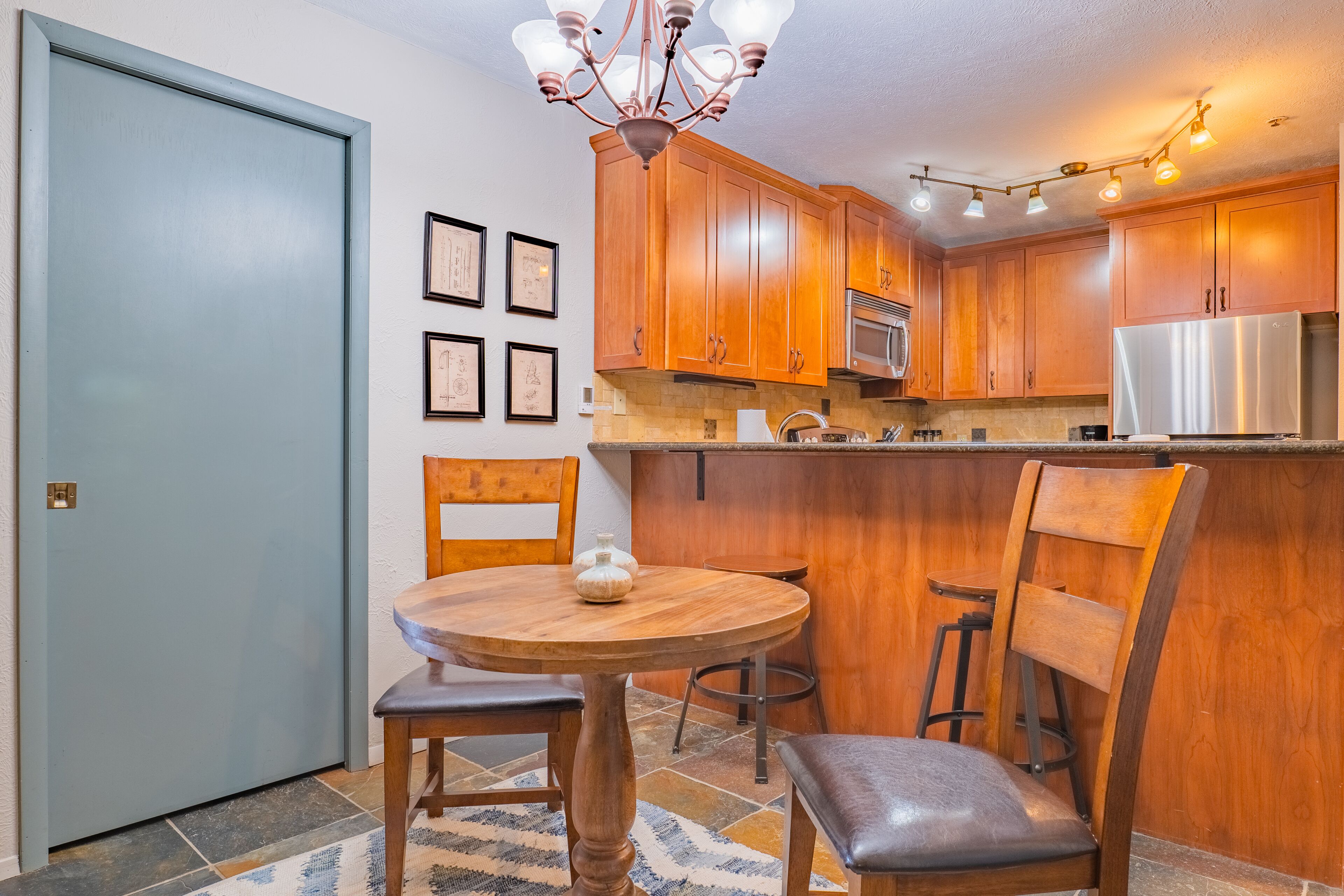 A kitchen with wooden cabinets, a stainless steel refrigerator, a chandelier, and a dining table with chairs.