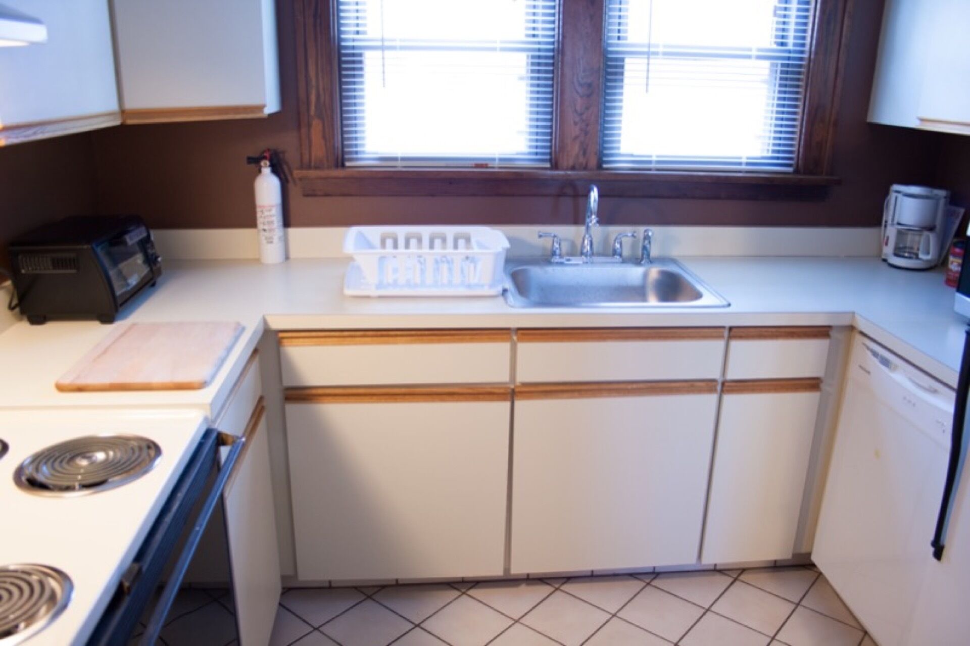 Een kleine keuken met een spoelbak, kookplaat en een raam met zonwering.
