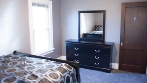 A bedroom with a bed, a dresser, a mirror, and a door.
