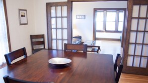A traditional Japanese-style dining room with a wooden table and chairs, a large window, and a view of a living area.