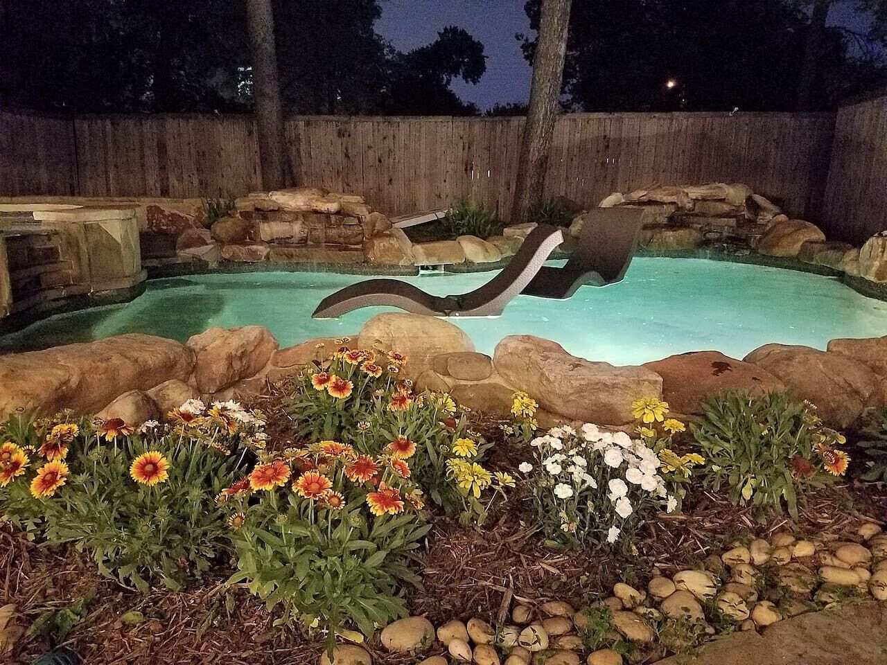 Una piscina con borde de rocas y diversas flores al frente.
