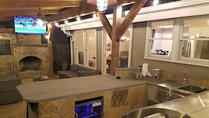 Een buitenkeuken van natuursteen met een barbecue, een ingebouwde oven en een aan de muur bevestigde televisie.