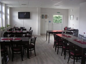 A dining area with multiple tables and chairs, a flat-screen TV mounted on the wall, and a window with a view of greenery.