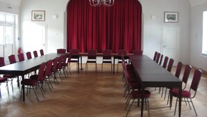A conference room with a long table and chairs, a red curtain backdrop, and a chandelier. - Hotel Langstedt (Langstedt)