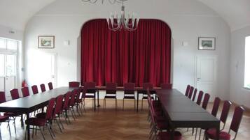 Un salón de conferencias con una larga mesa y sillas, un telón rojo de fondo y una araña.