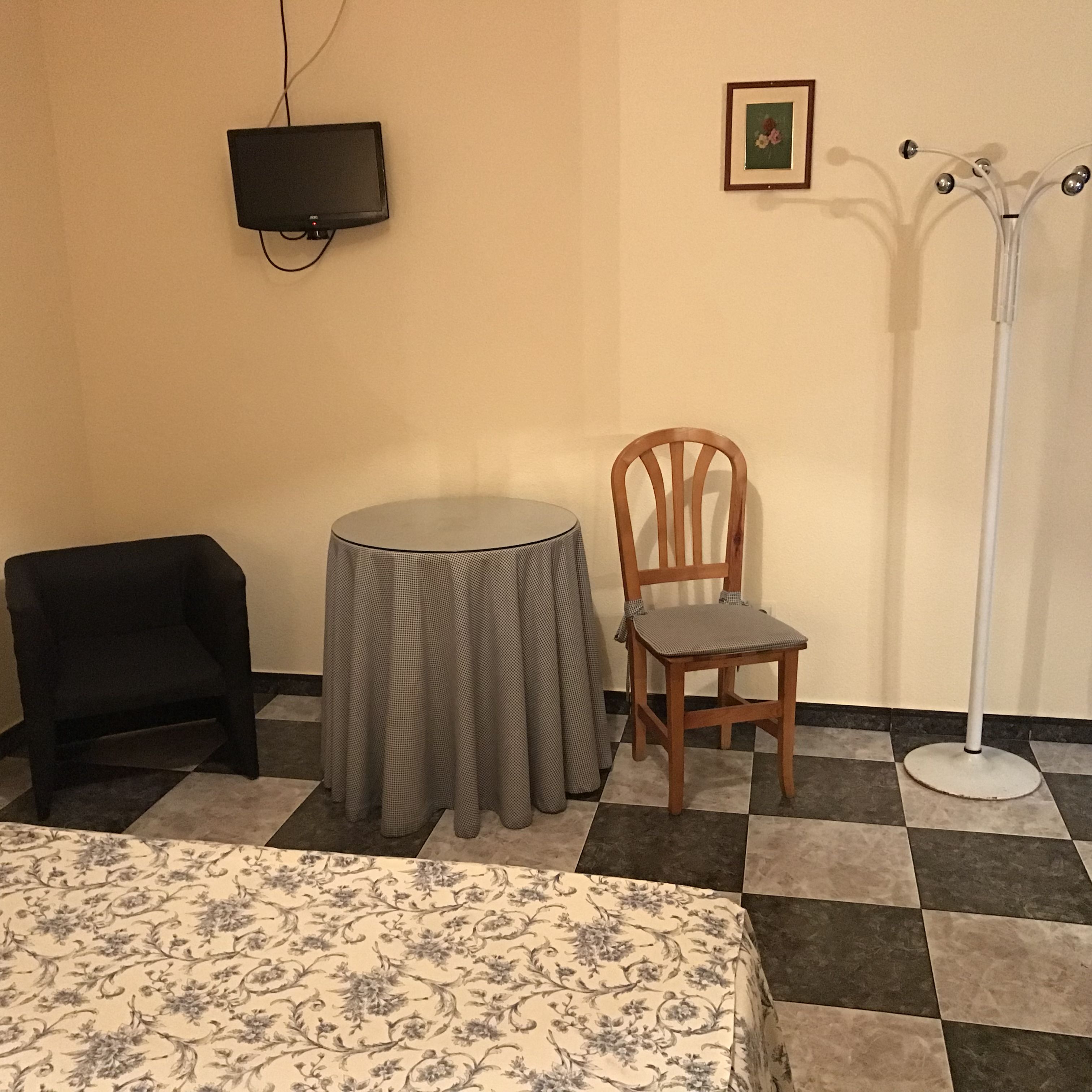 Una habitación con cama, una mesita redonda pequeña, una silla, un televisor y un perchero.