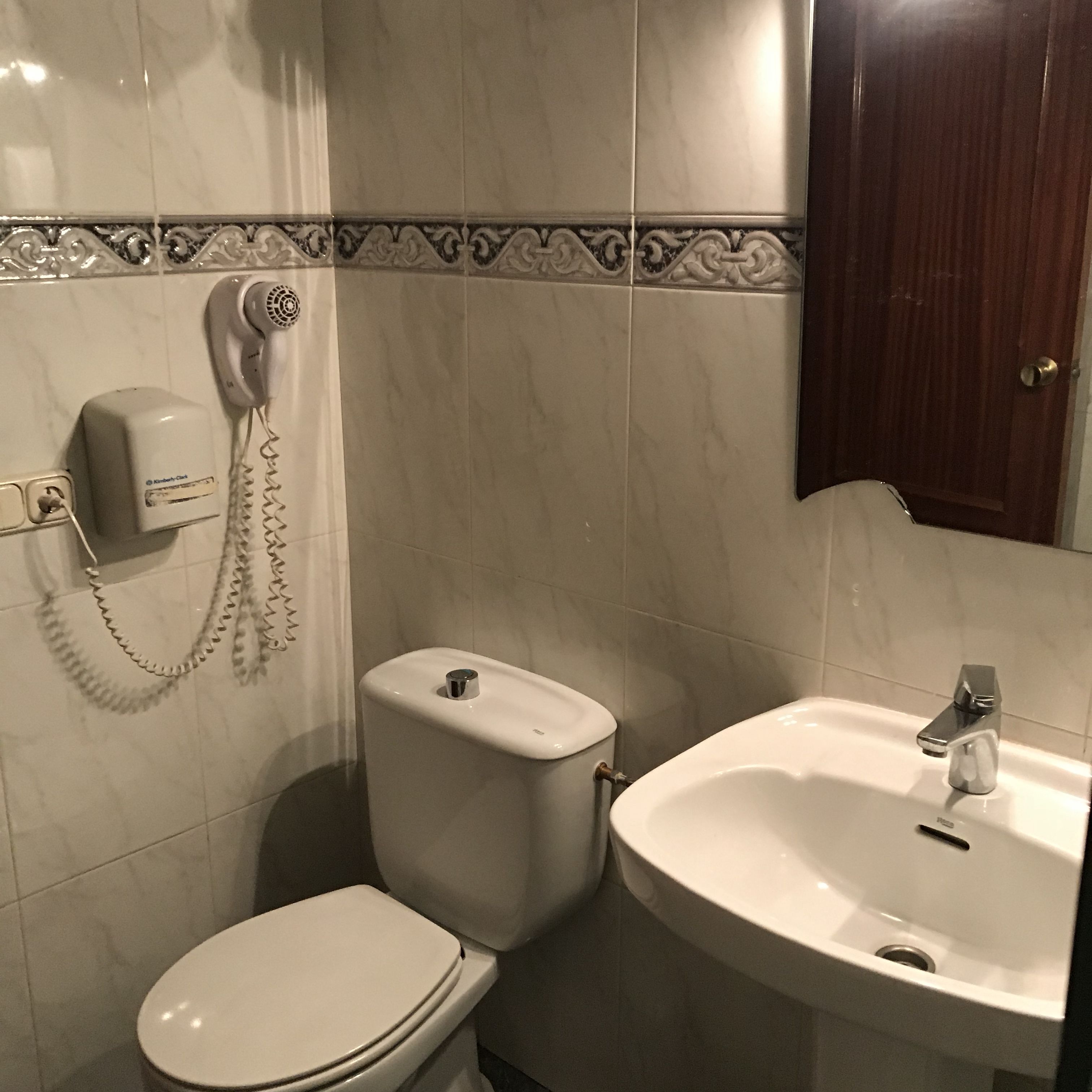 A bathroom with a toilet, a sink, and a hairdryer mounted on the wall.