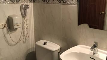 A bathroom with a toilet, a sink, and a hairdryer mounted on the wall.