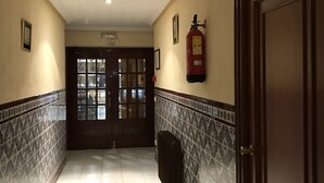 A hallway with a fire extinguisher mounted on the wall, a door with the number 210, and a tiled floor. - Santa Ana Hostal (Madridejos)