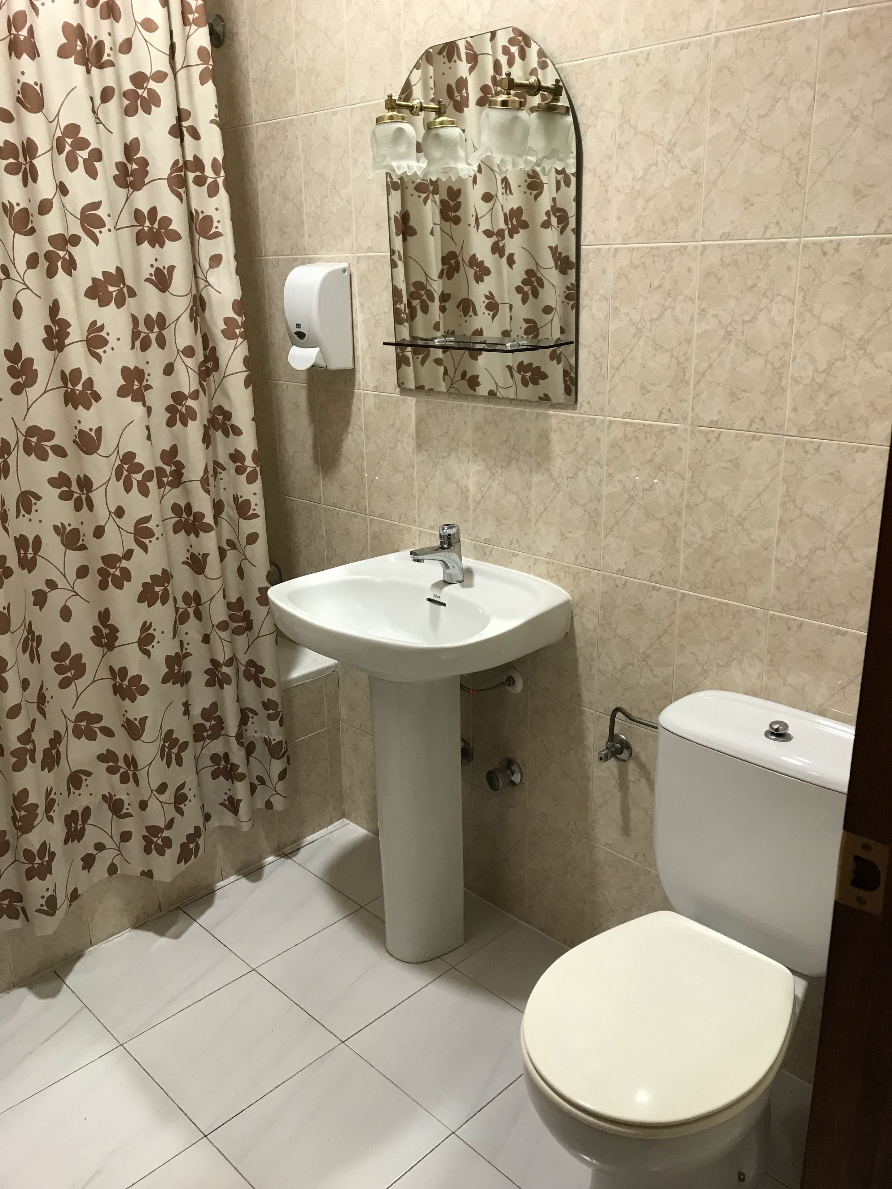Et badeværelse med en hvid vask, toilet og et bruseforhæng med blomstermønster.