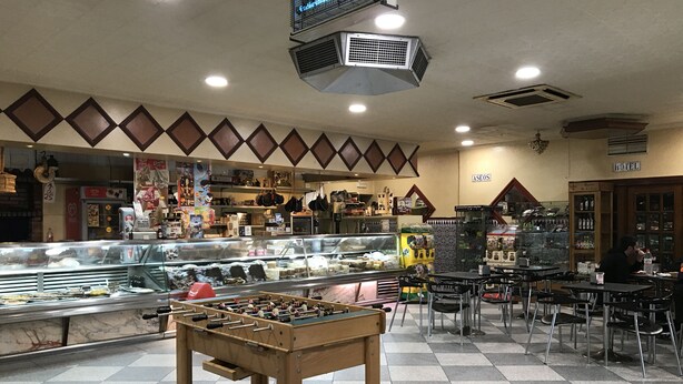 A hotel lobby with a foosball table, a glass display case with food items, and a seating area with tables and chairs. - Santa Ana Hostal (Madridejos)