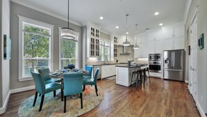 A modern kitchen with white cabinetry, stainless steel appliances, and a dining area with teal chairs and a round table.