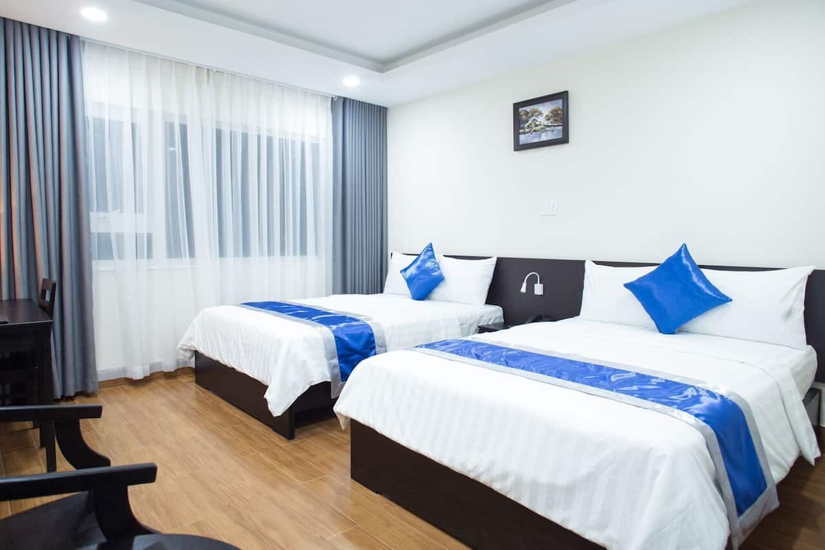 A hotel room with two beds, a desk, and a window with curtains.