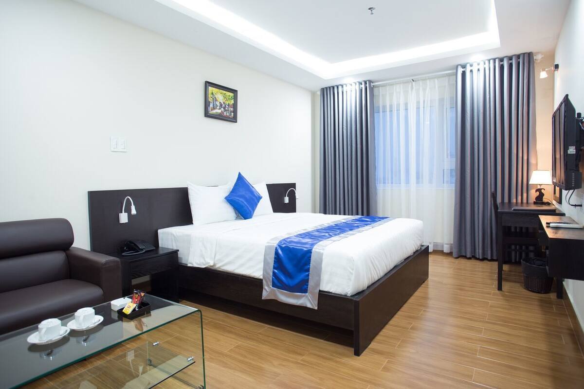 A modern hotel room with a large bed, a sofa, a glass coffee table, a desk, and a TV.
