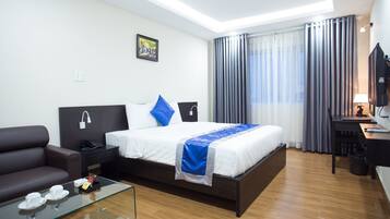 A modern hotel room with a large bed, a sofa, a glass coffee table, a desk, and a TV.
