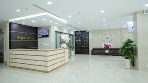 A hotel reception area with a reception desk, a clock, and potted plants. - SoLex Hotel (Ho Chi Minh City)