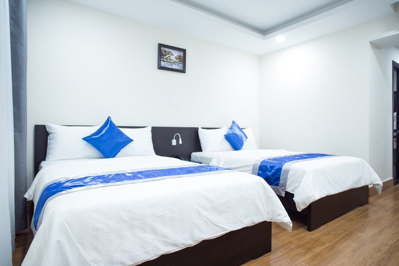 A hotel room with two beds, white bedding, blue accents, a picture on the wall, and a wooden floor.