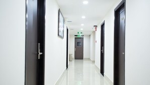 A hallway with black doors, white walls, and a shiny floor. There is a door at the end with a green exit sign above it. - SoLex Hotel (Ho Chi Minh City)