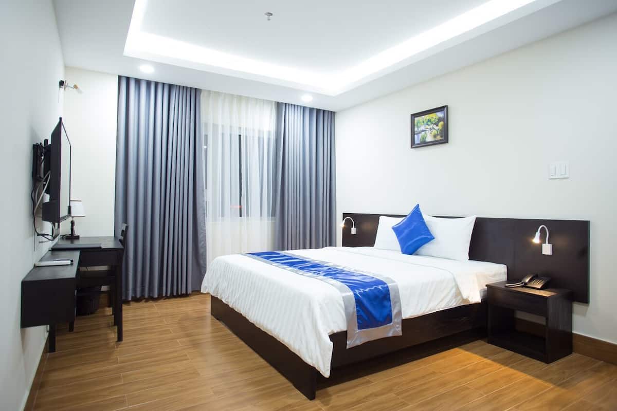 A modern hotel room with a large bed, a desk, a chair, a TV, and a picture on the wall.