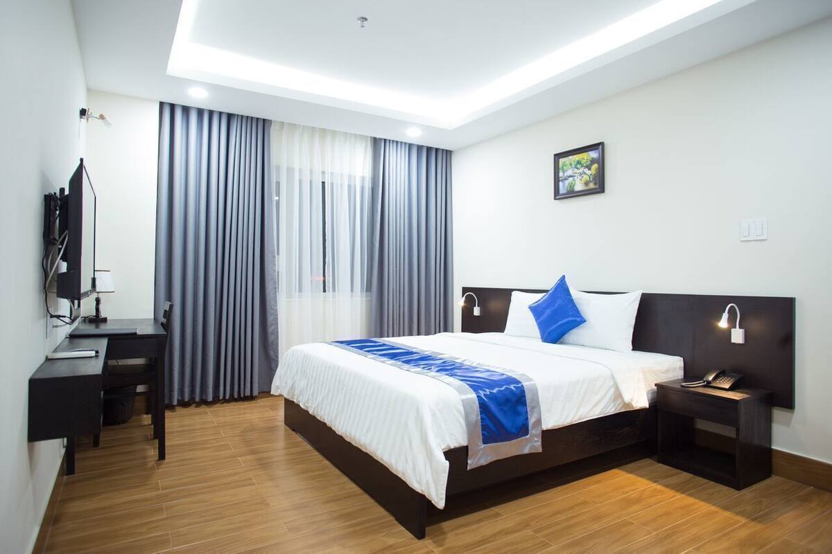 A modern hotel room with a bed, bedside tables, a desk, and a TV.