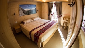 Un dormitorio de madera con una cama, un cuadro de una montaña, una mesita de noche pequeña y una ventana con cortinas.