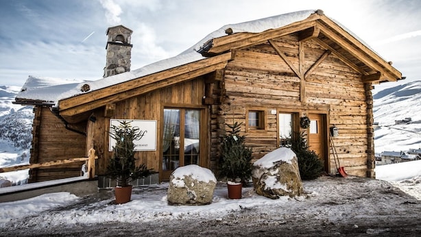 Una cabaña de madera con techo nevado, chimenea y un cartel que indica que es un restaurante.