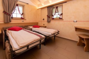 A room with two beds, each with a red pillow, wooden headboards, and a small wooden table. - Al Solif Bed & Breakfast (Livigno)