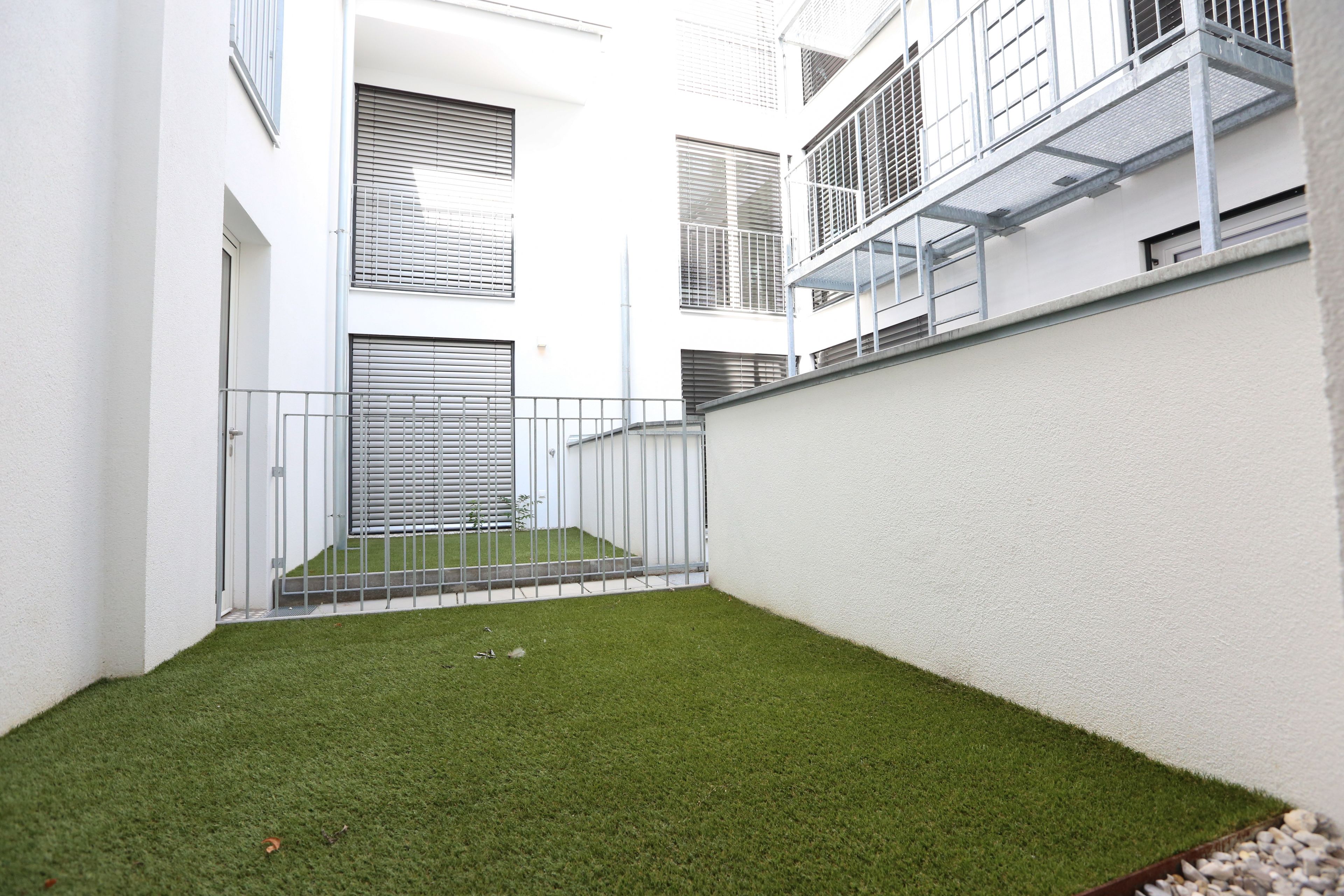 Une cour avec une pelouse artificielle, des murs blancs et des rampes en métal.