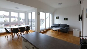 Un espacio habitable moderno con comedor, sofá y ventanas amplias con vistas a la ciudad.