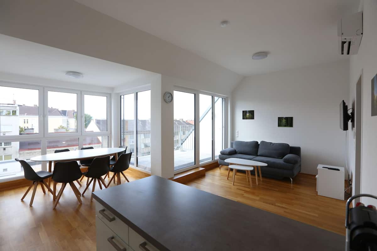 A modern living space with a dining area, a sofa, and large windows offering views of the city.