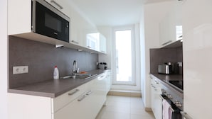 Una cocina moderna con armarios blancos, microondas integrado, horno de acero inoxidable y ventana que proporciona luz natural.