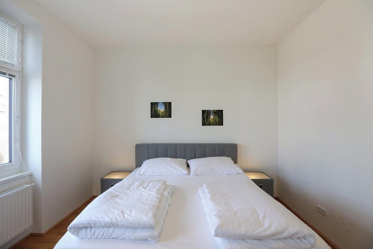 A bedroom with a bed, two bedside tables, a window, and two wall-mounted pictures.