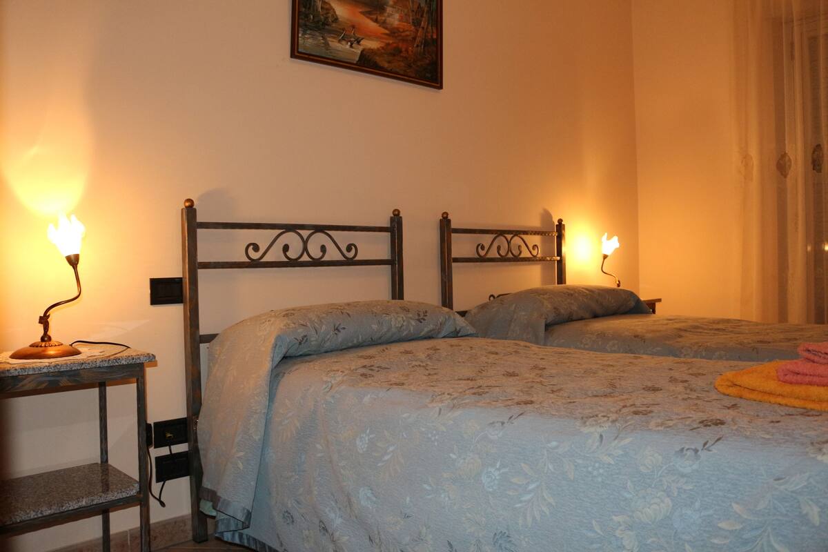 A hotel room with two beds, a nightstand, and a painting on the wall.