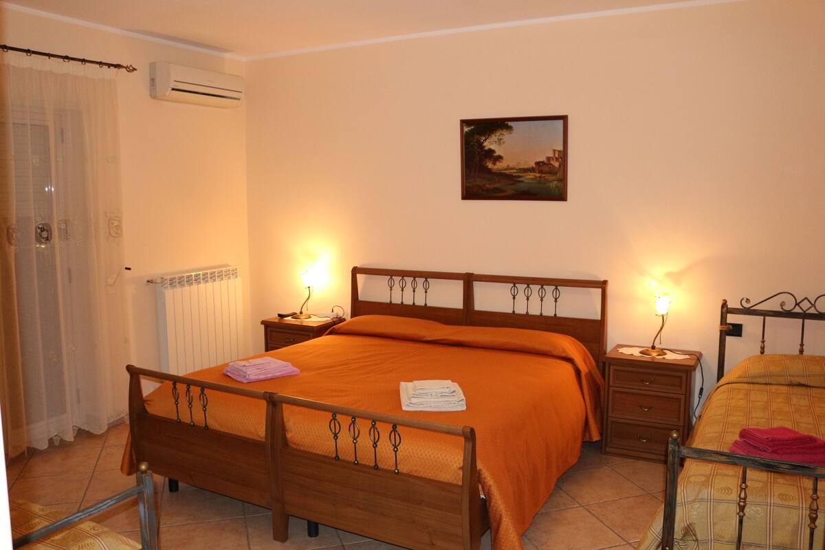 A bedroom with a wooden bed, two bedside tables with lamps, a radiator, and a painting on the wall.