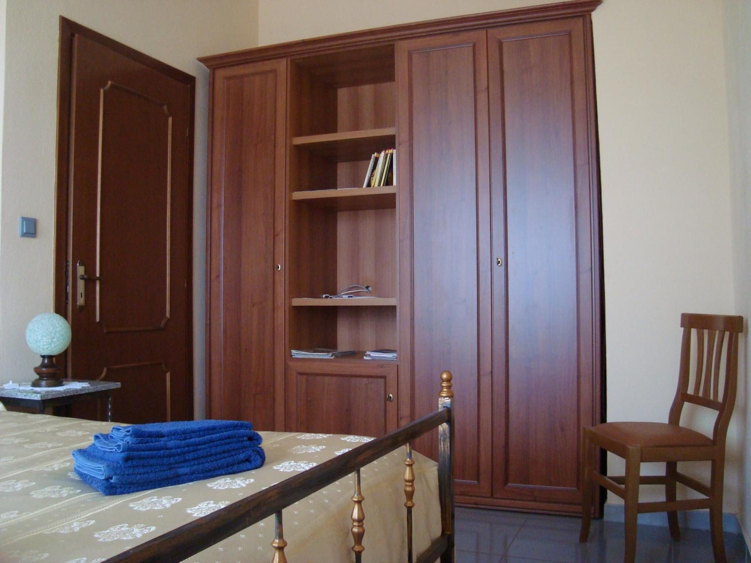 Un dormitorio con cama, armario de madera, una silla y una mesita con un globo terráqueo.