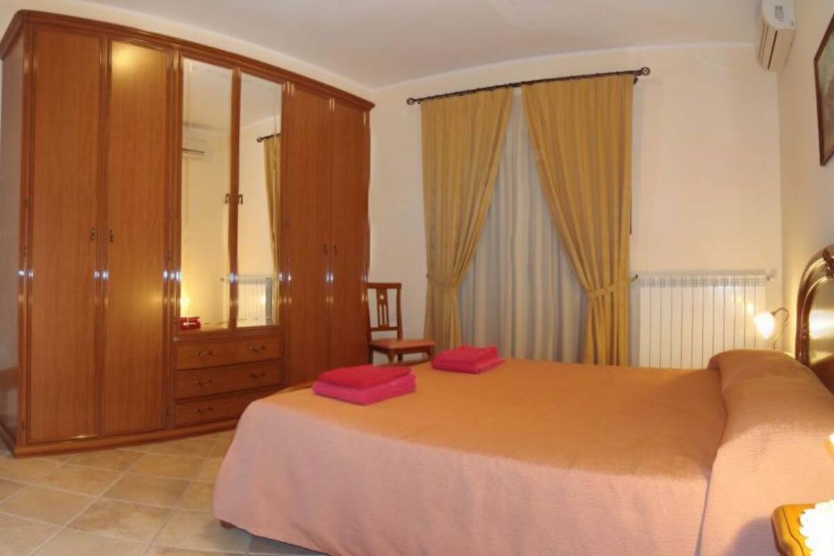 A bedroom with a large bed, a wardrobe, a mirror, a table, and curtains.