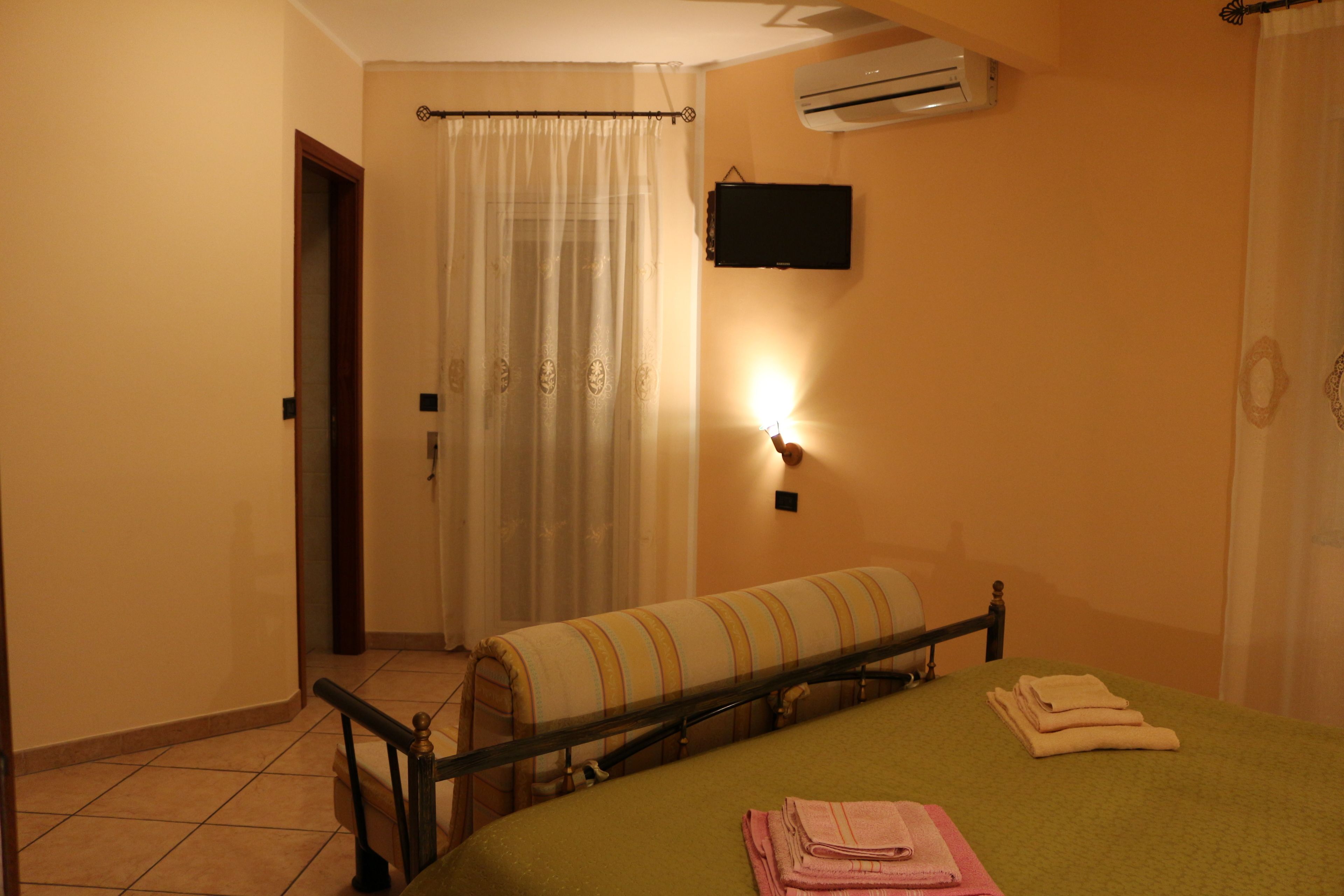 A room with a bed, a bench, a wall-mounted TV, and an air conditioner.