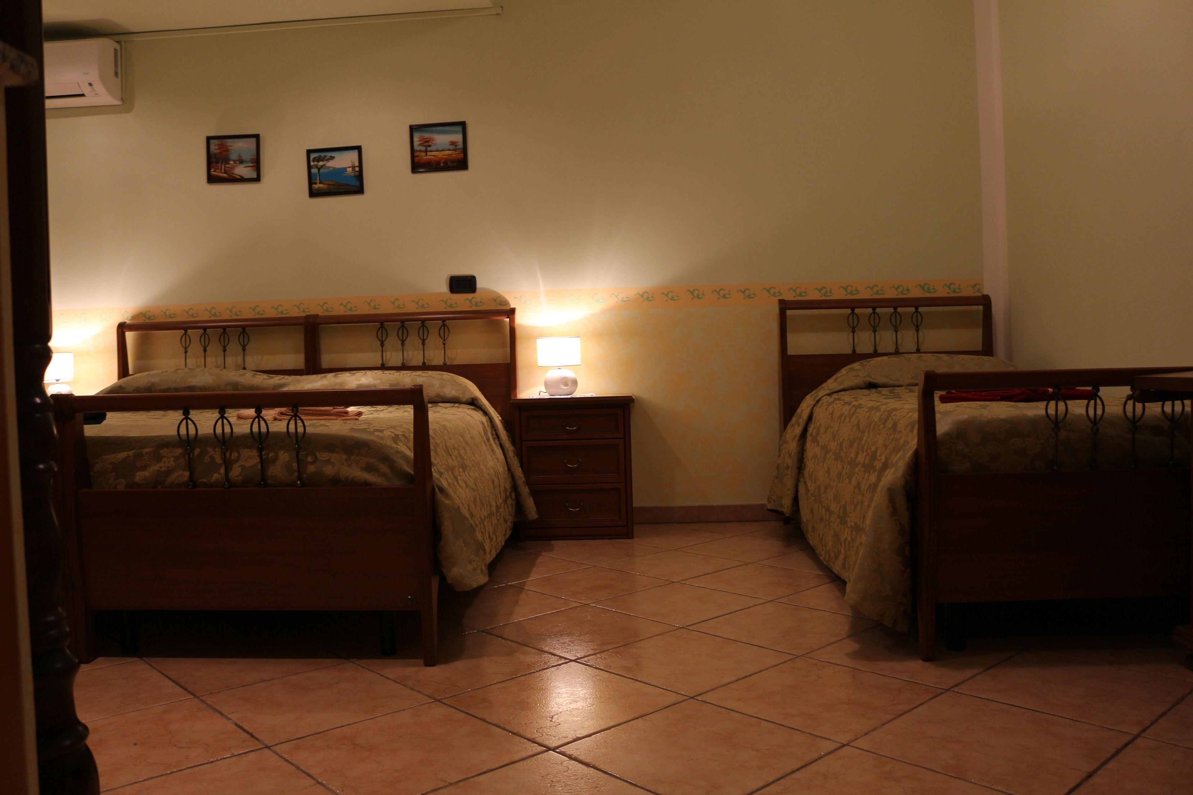 A bedroom with two beds, a bedside table with a lamp, and three framed pictures on the wall.