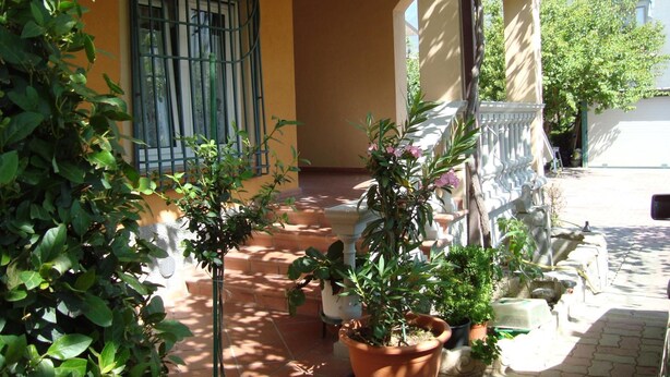 A courtyard with potted plants, a tiled floor, and a building with a barred window. - B&B Esperanca (Frascineto)
