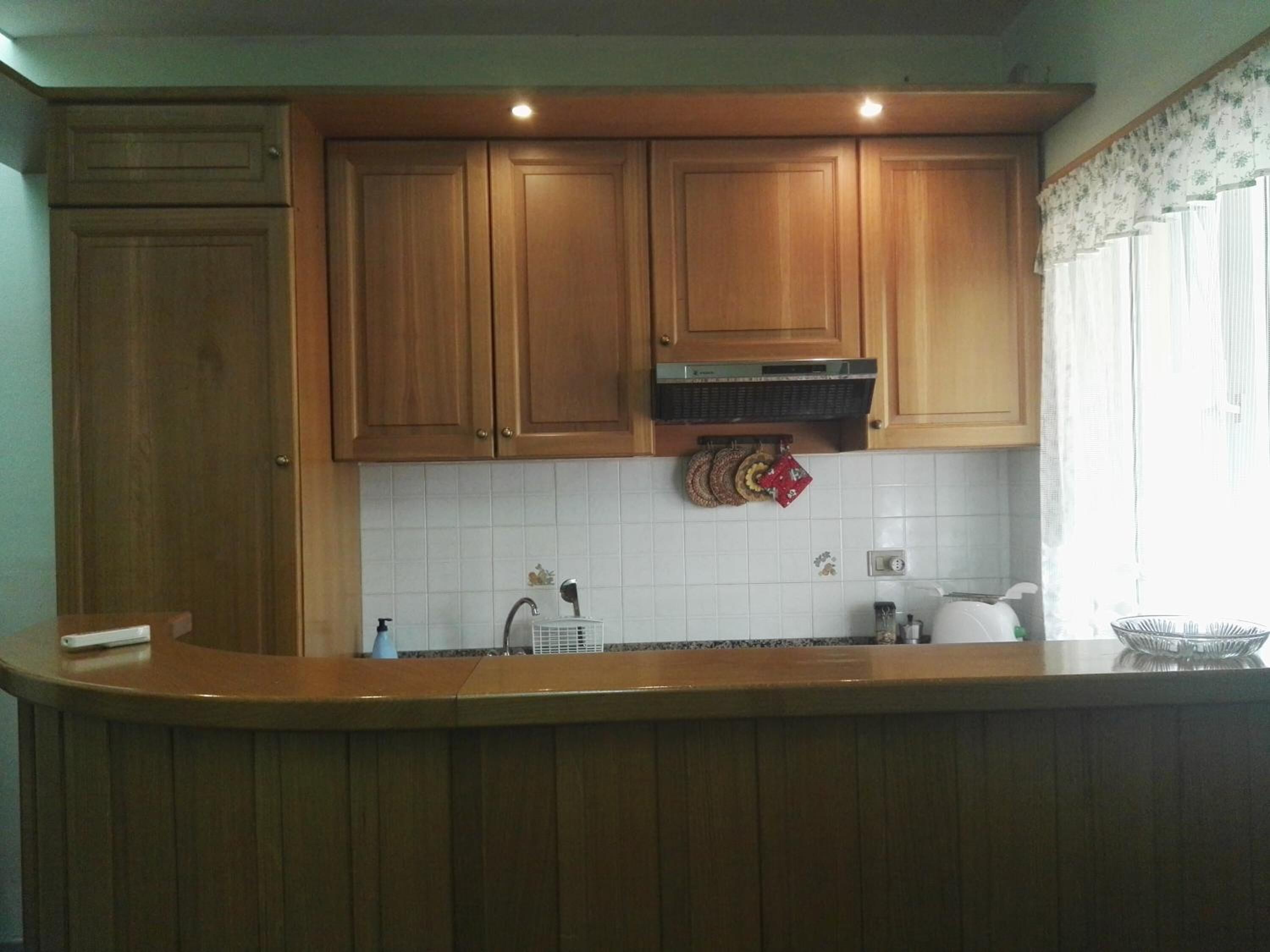 A kitchen with wooden cabinets, a white tiled backsplash, a stainless steel sink, and a window with a floral curtain.