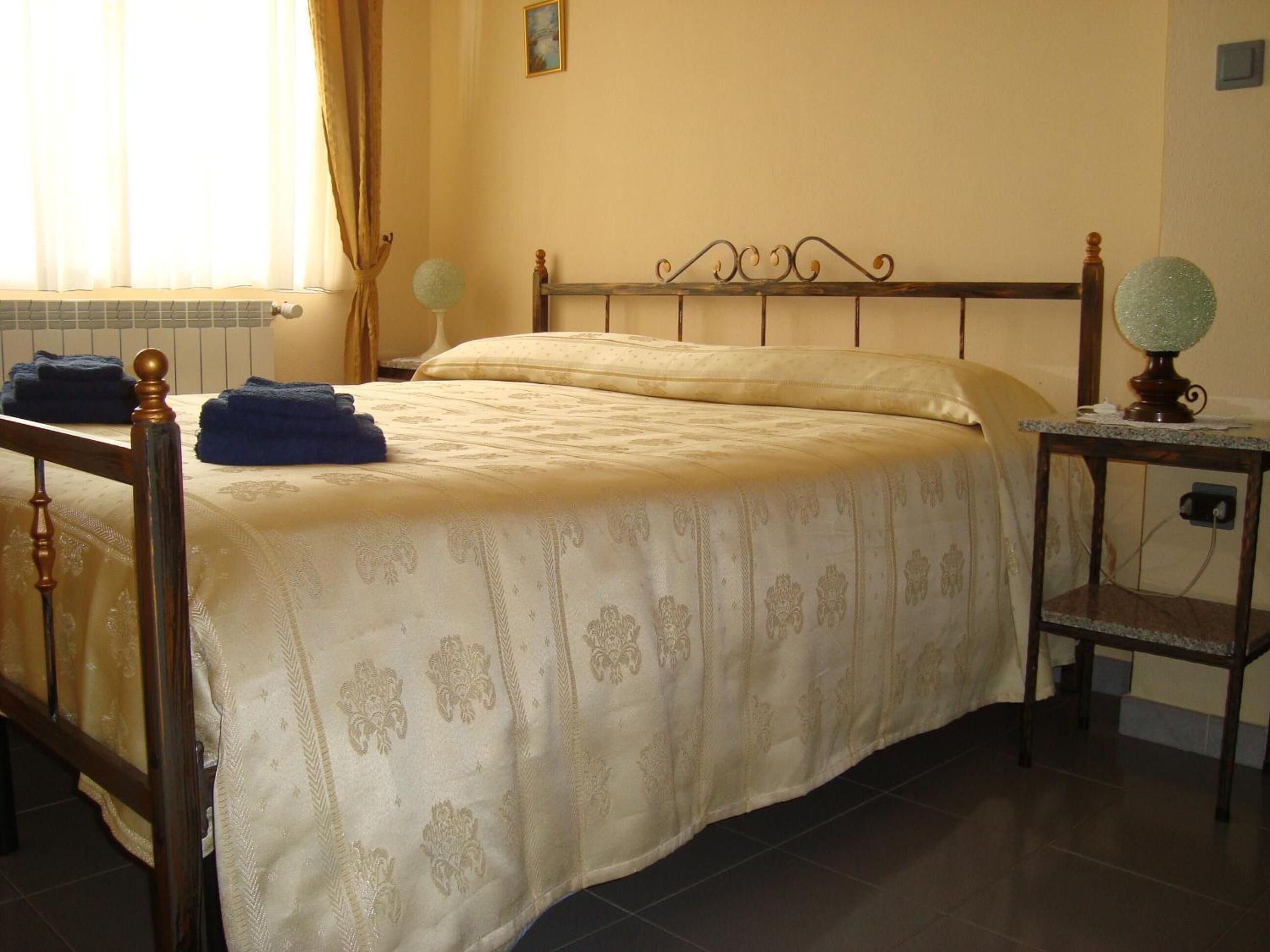 Un dormitorio con cama, mesita de noche, lámpara y ventana con cortinas.