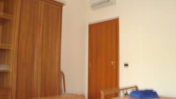 A bedroom with a wooden wardrobe, a bed with a pink bedspread, and a blue towel on the bed.