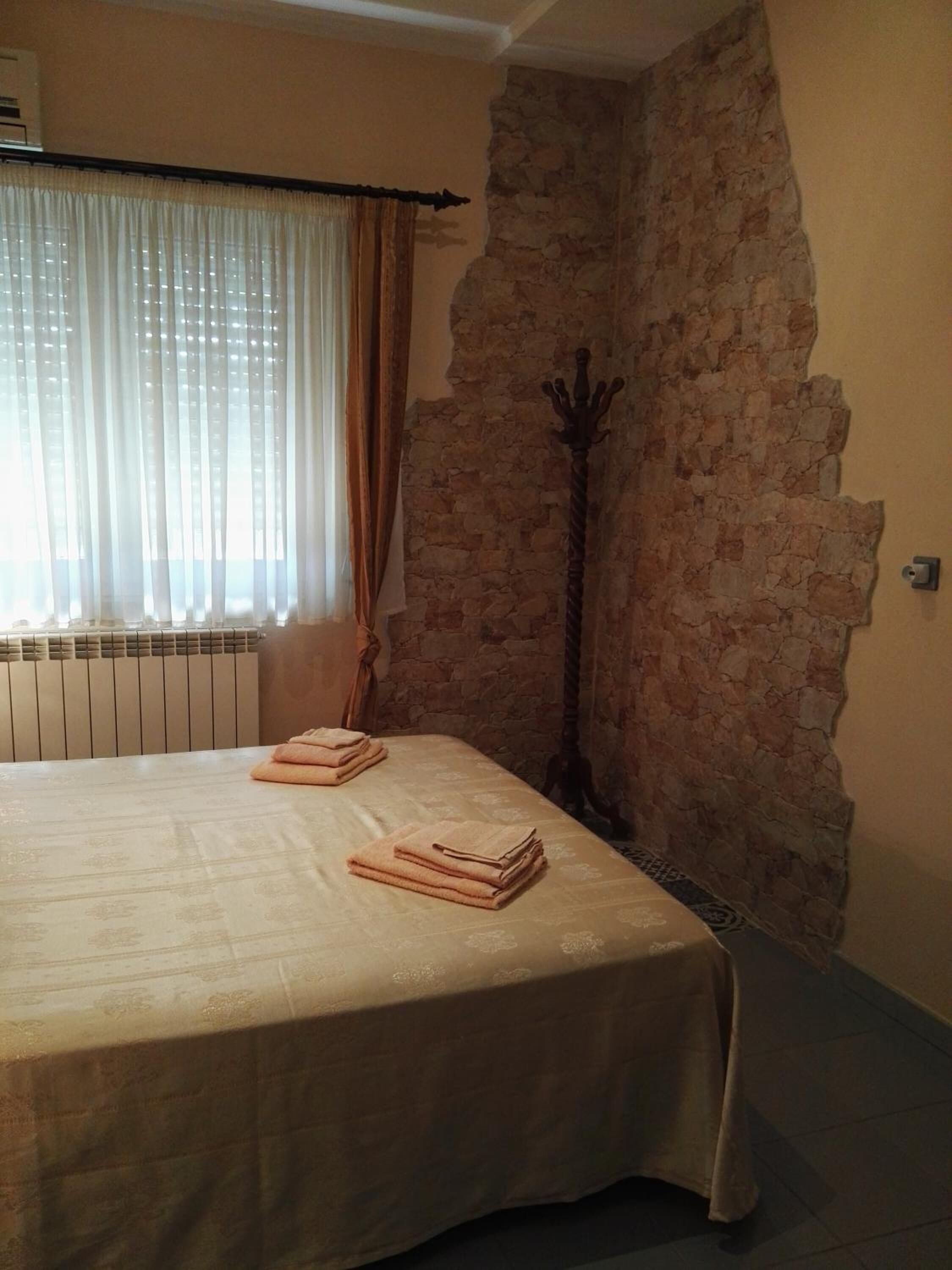 Une pièce avec un lit, un radiateur, un mur en pierre et un porte-manteau.