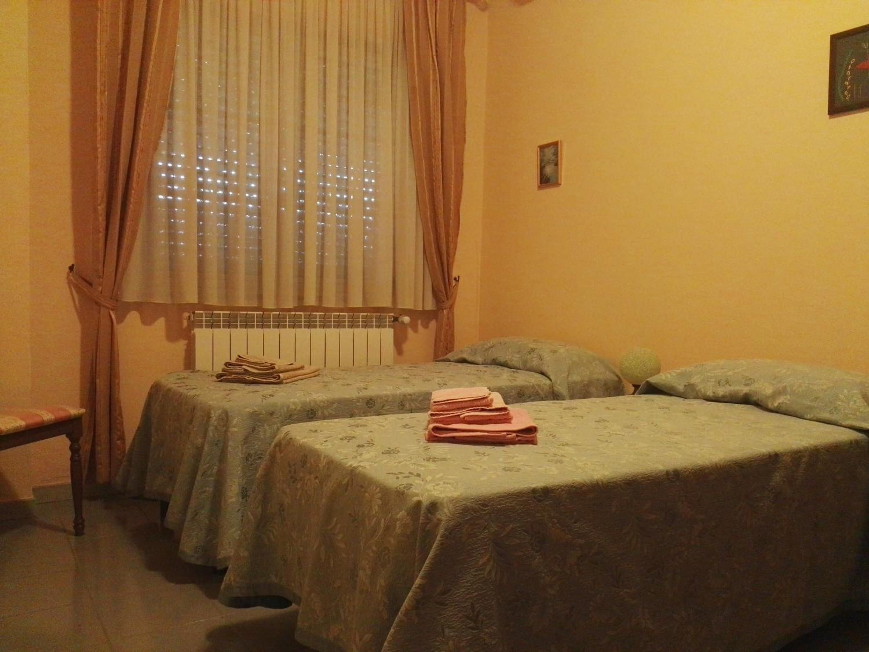 A room with two single beds, a radiator, and a window with curtains.