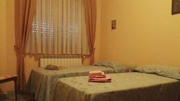 A room with two single beds, a radiator, and a window with curtains.