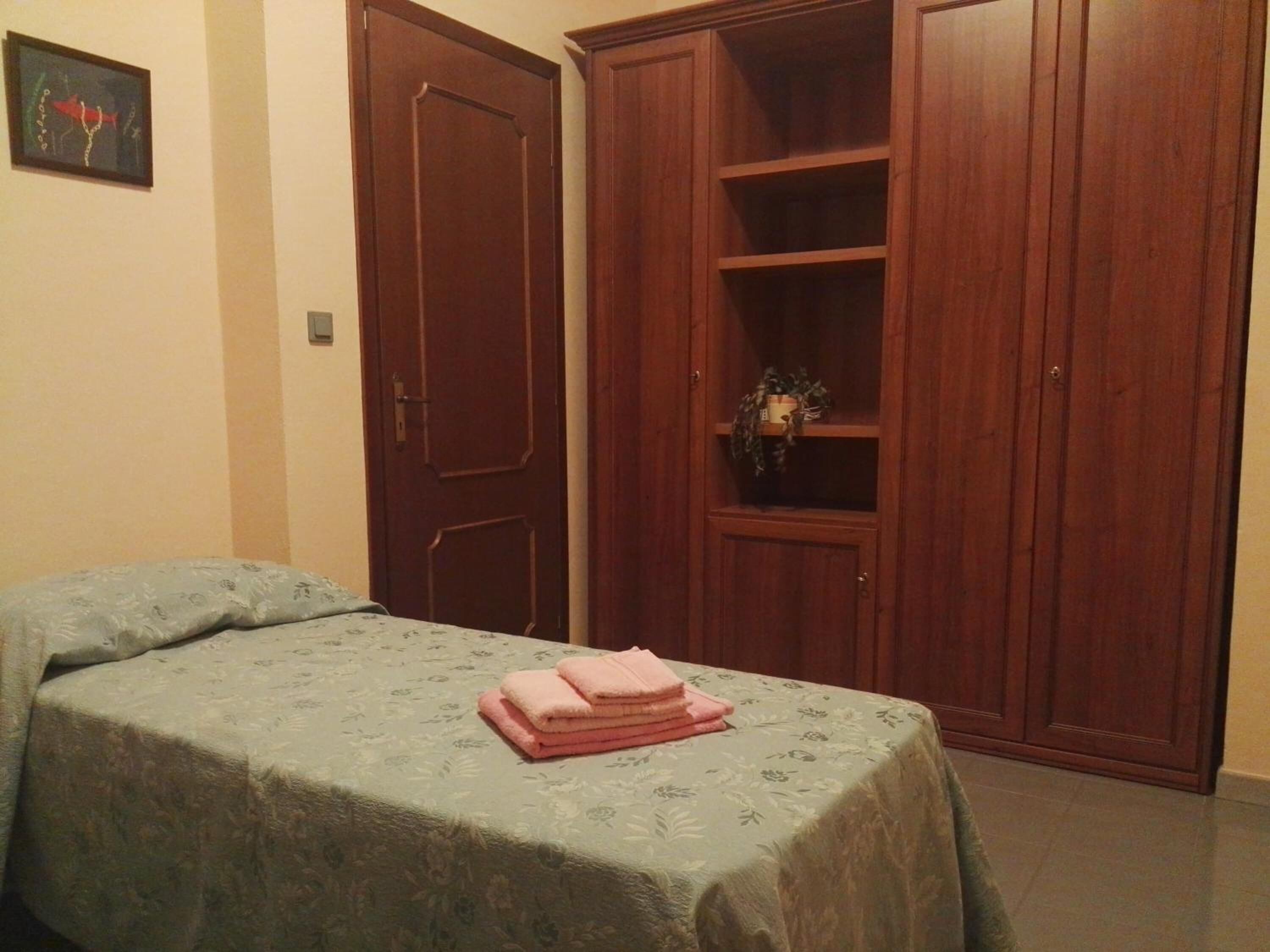 Un dormitorio con cama, un armario de madera y una estantería con una planta.